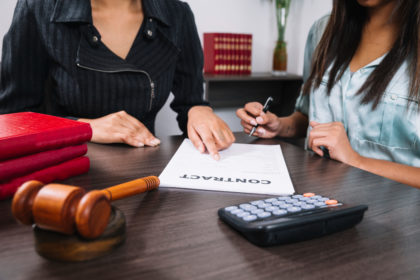 black-woman-pointing-document-near-lady-with-pen-table-with-calculator-gavel